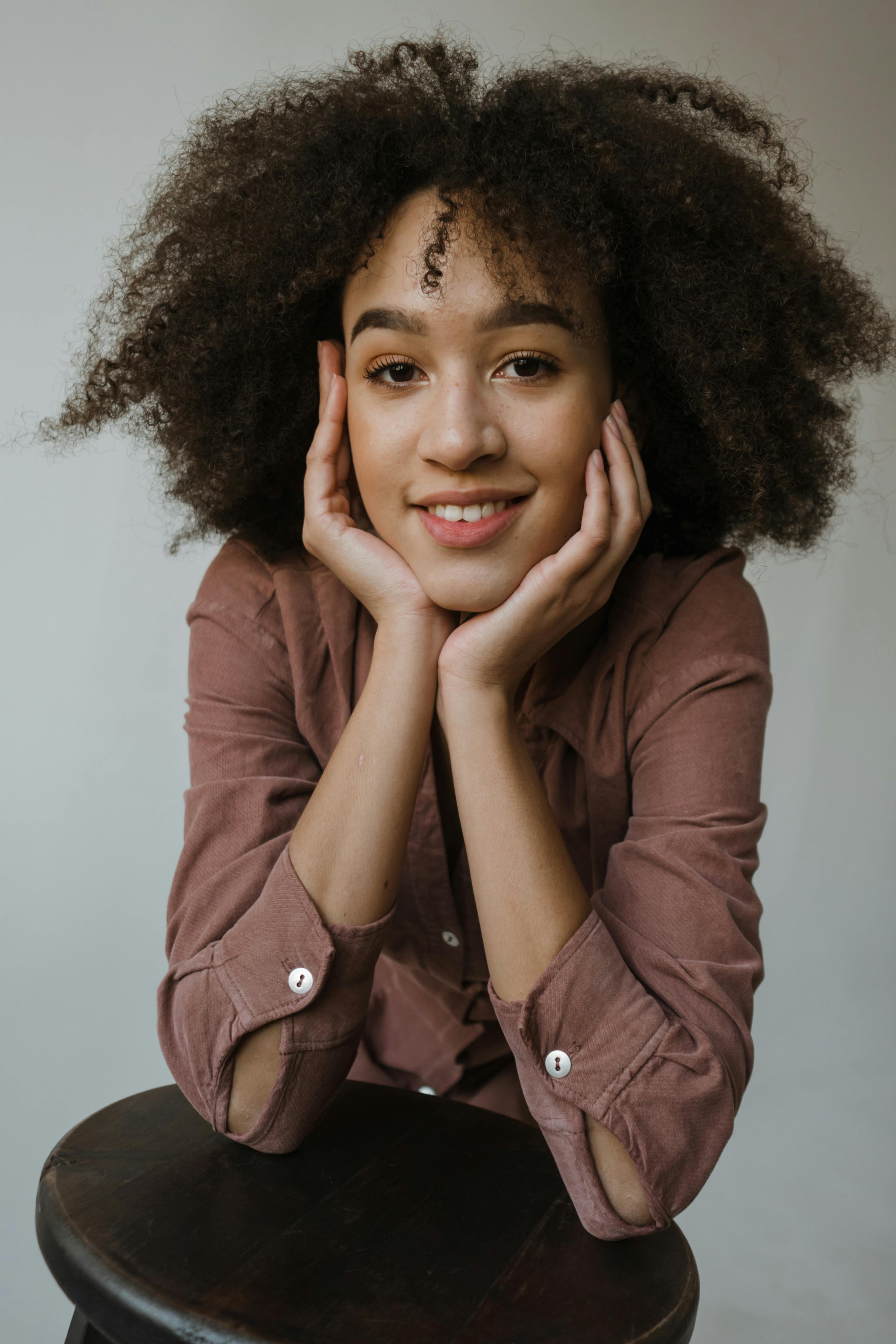 Studio portrait of a young woman with curly hair and a warm smile, exemplifying natural beauty and style.