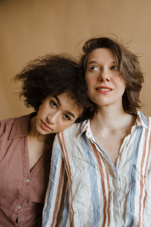 Free Portrait of two women posing in a studio with a warm backdrop, showcasing stylish striped and plain tops. Stock Photo