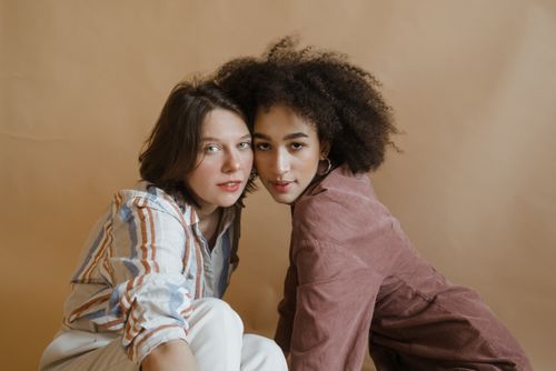 Free Two young women, one with curly afro hair and the other with straight hair, posing indoors against a brown backdrop. Stock Photo