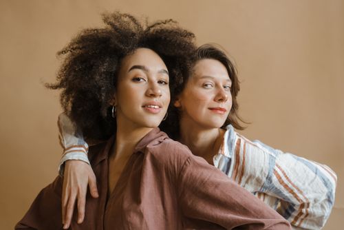 Free Portrait featuring two diverse women smiling and embracing in a studio setting, symbolizing friendship and empowerment. Stock Photo