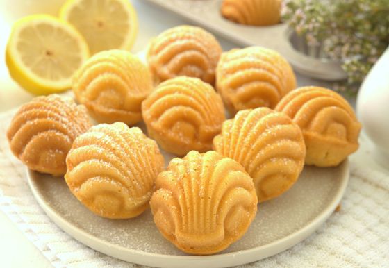 Plate of golden shell-shaped madeleines lightly sugared, with lemon slices and a madeleine pan