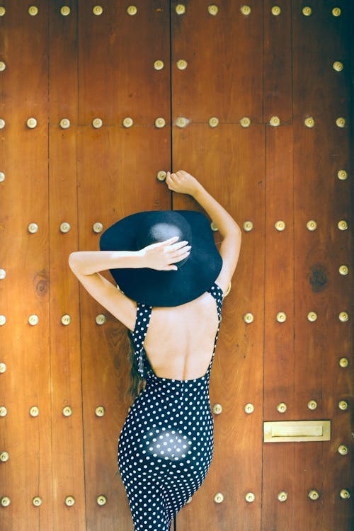 Mujer En Vestido De Lunares Blanco Y Negro Apoyado En La Pared De Madera Marrón