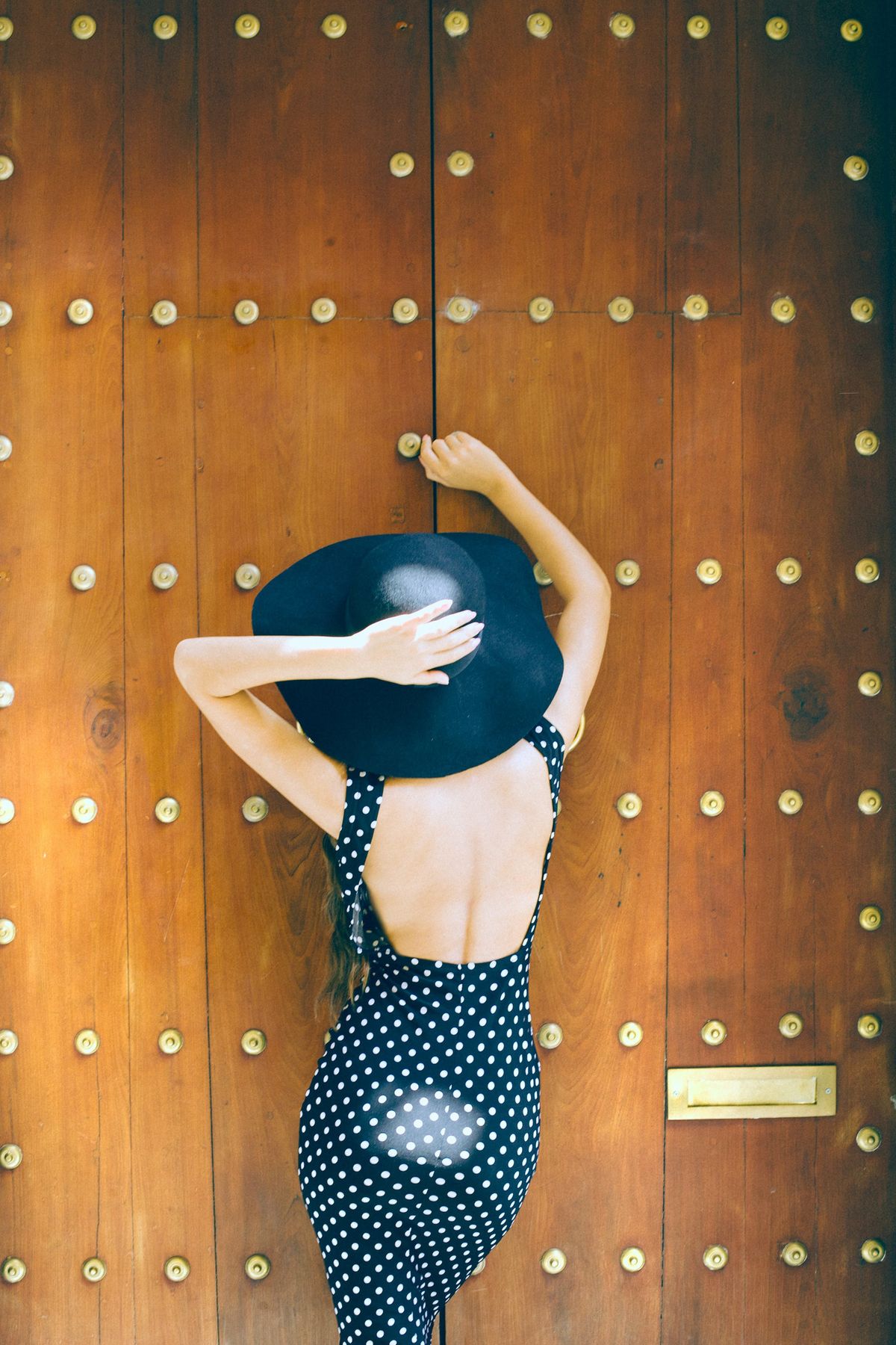 A woman in a hat standing near a wall — the sun-warmed mood of summer dots