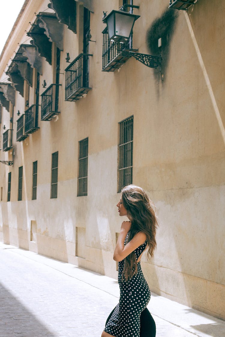 Stylish Woman In Dress Standing On Sidewalk Near Old Building