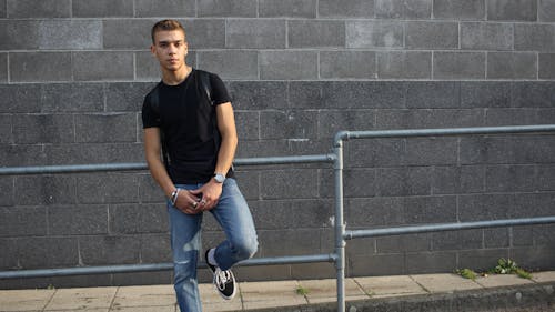 Man in Black Crew Neck T-shirt and Blue Denim Jeans Sitting on Gray Metal Railings