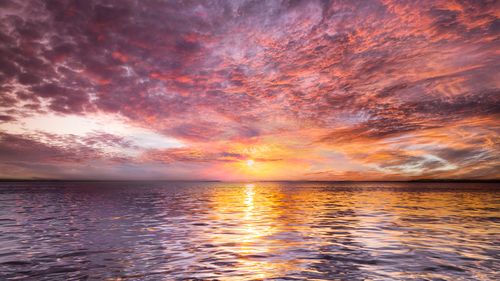 Free A breathtaking ocean sunset with colorful clouds and tranquil water reflection. Stock Photo