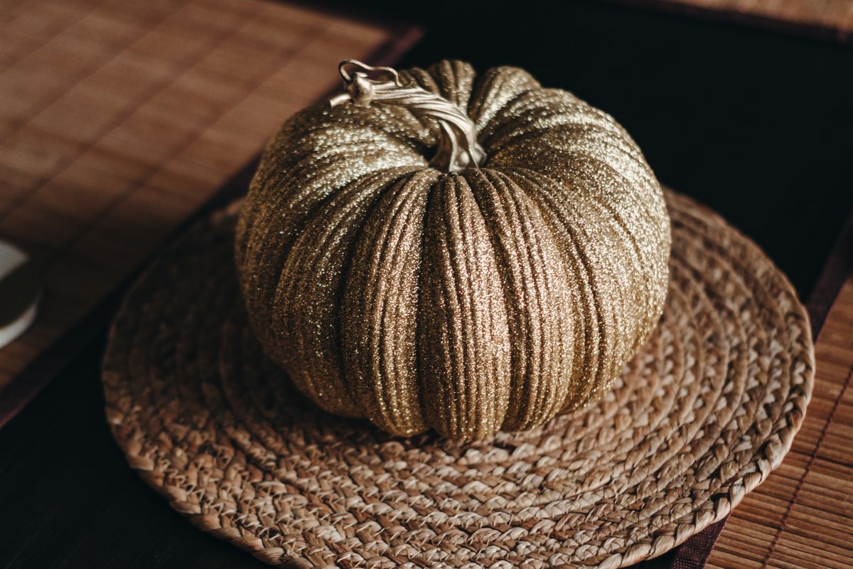 A shimmering gold pumpkin adorned with glitter sits elegantly on a woven mat, perfect for autumn décor. Stock Photo.