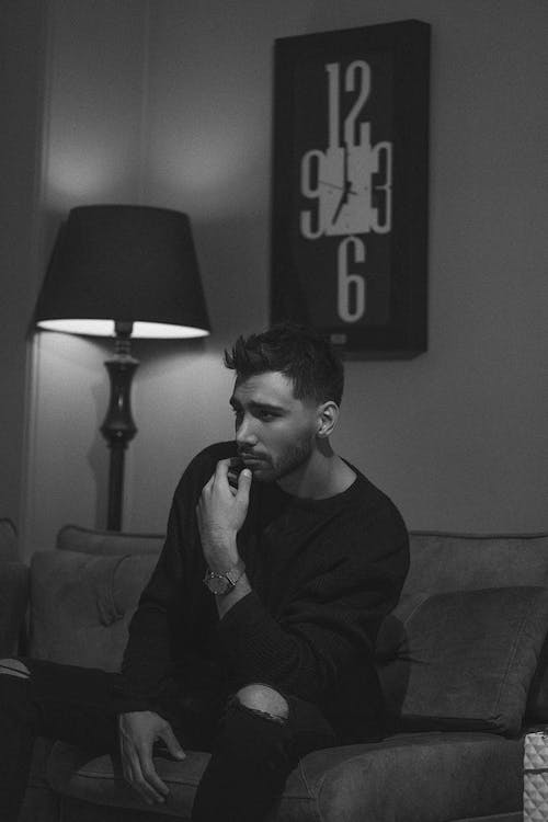 A Grayscale of a Man in a Black Sweater Sitting on a Couch