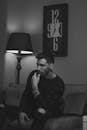 A Grayscale of a Man in a Black Sweater Sitting on a Couch