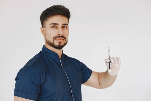 A bearded male healthcare worker in scrubs holding a syringe against a white background.