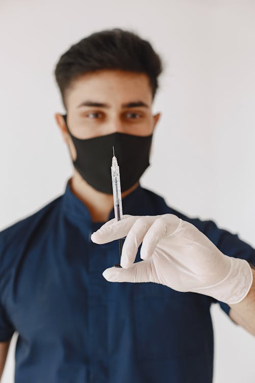 Man in Blue Uniform with Black Face Mask Holding a Syringe