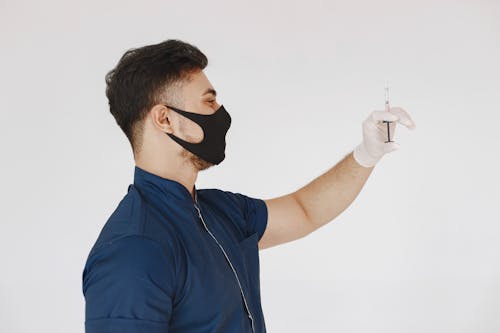 Man in Blue Uniform with Black Face Mask Holding a Syringe