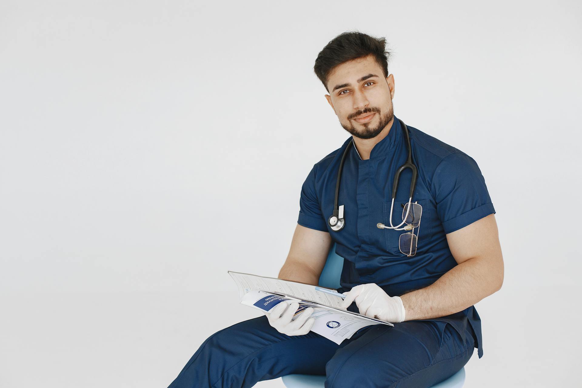 Young male doctor in blue scrubs reviewing medical records with a confident smile.