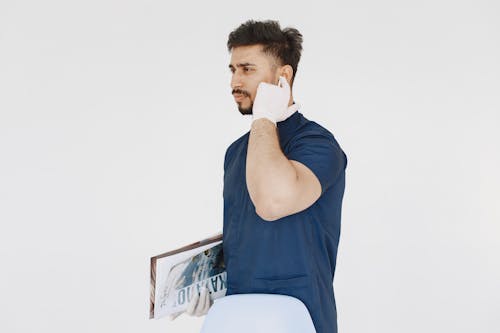 Man in Blue Scrub Suit Holding His Ear Pods