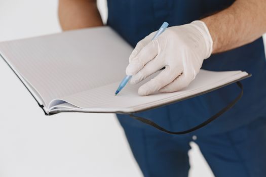 A healthcare worker in gloves writing notes on a notebook indoors.