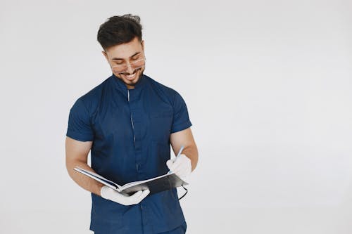 Man in Blue Scrub Suit Writing on a Book