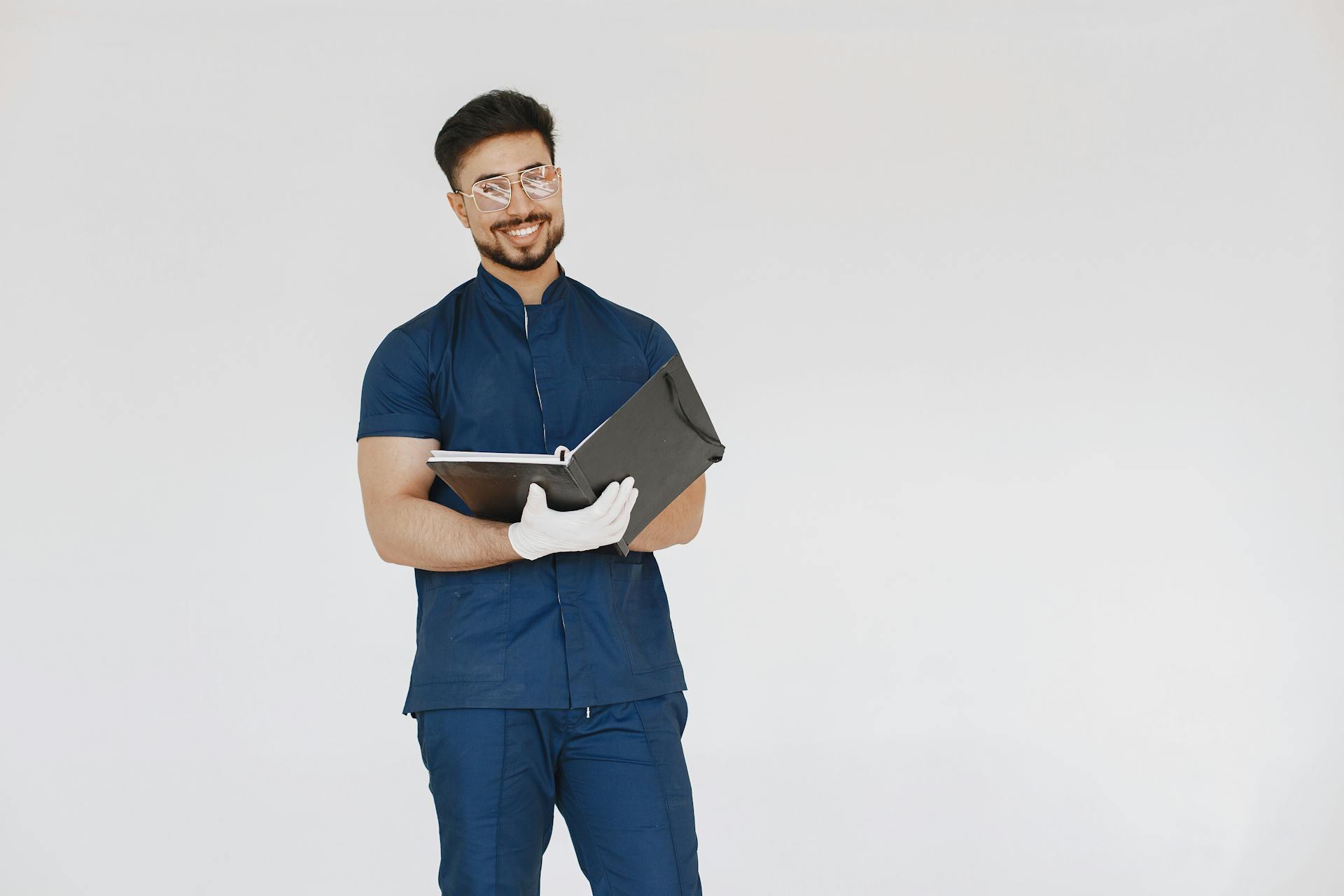 A cheerful medical professional in scrubs with latex gloves, holding a black file folder.