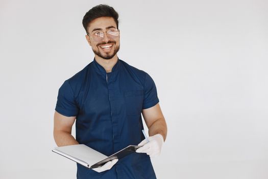 A cheerful medical professional in blue scrubs holding a notebook, wearing glasses and white gloves.