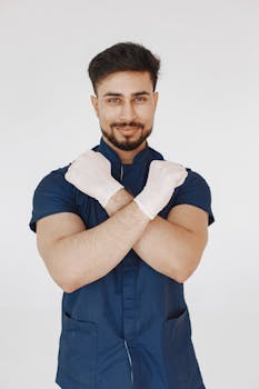 Confident male healthcare worker posing with crossed arms, wearing gloves on a white background.