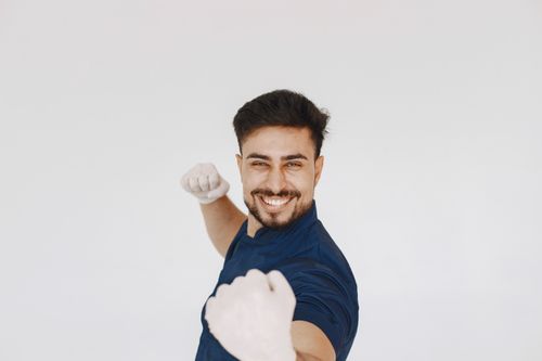 Free A cheerful man with a beard raises his fists playfully against a white studio backdrop. Stock Photo