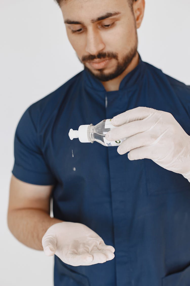 Man In Blue Scrub Suit Sanitizing His Hands