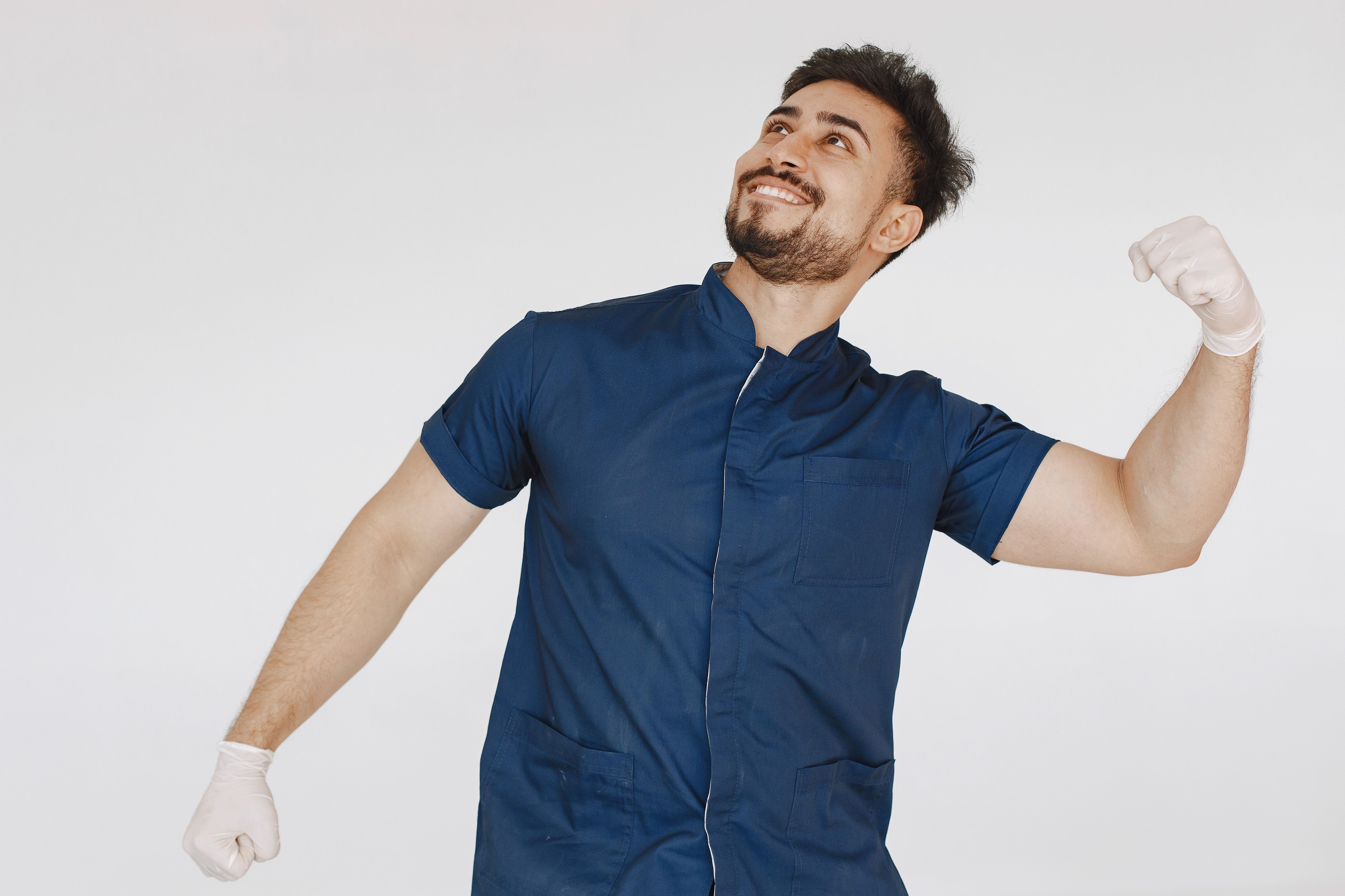 Smiling male medical professional in blue scrub suit poses confidently against a plain white background.
