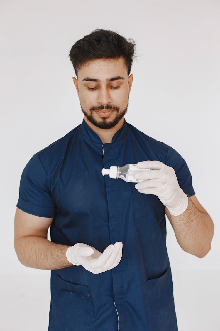 Man In Blue Scrub Suit Sanitizing His Hands