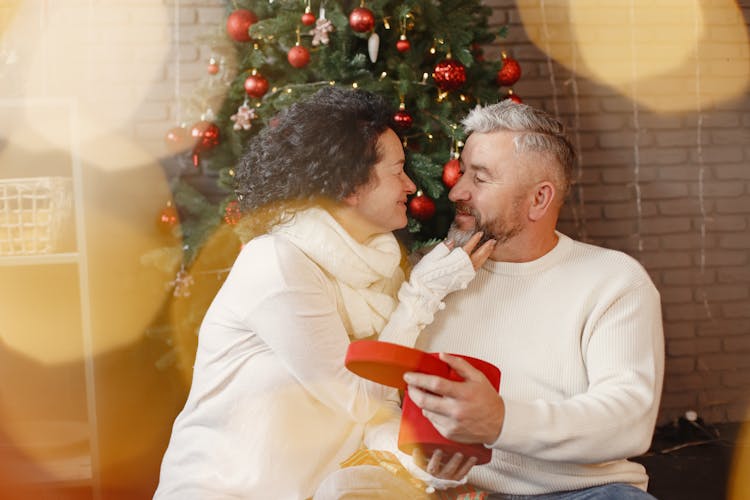 Happy Elderly Couple Sitting Next To A Christmas Tree