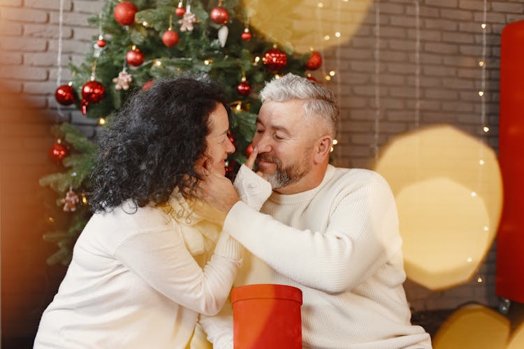 Happy Elderly Couple Sitting Next To A Christmas Tree