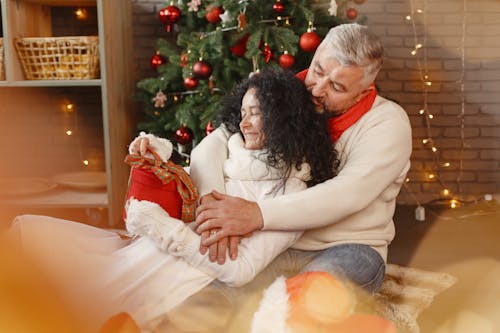 Free Elderly Couple Hugging while Sitting Beside the Christmas Tree Stock Photo