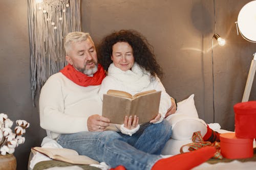 Elderly Couple Reading Book while Sitting on the Bed