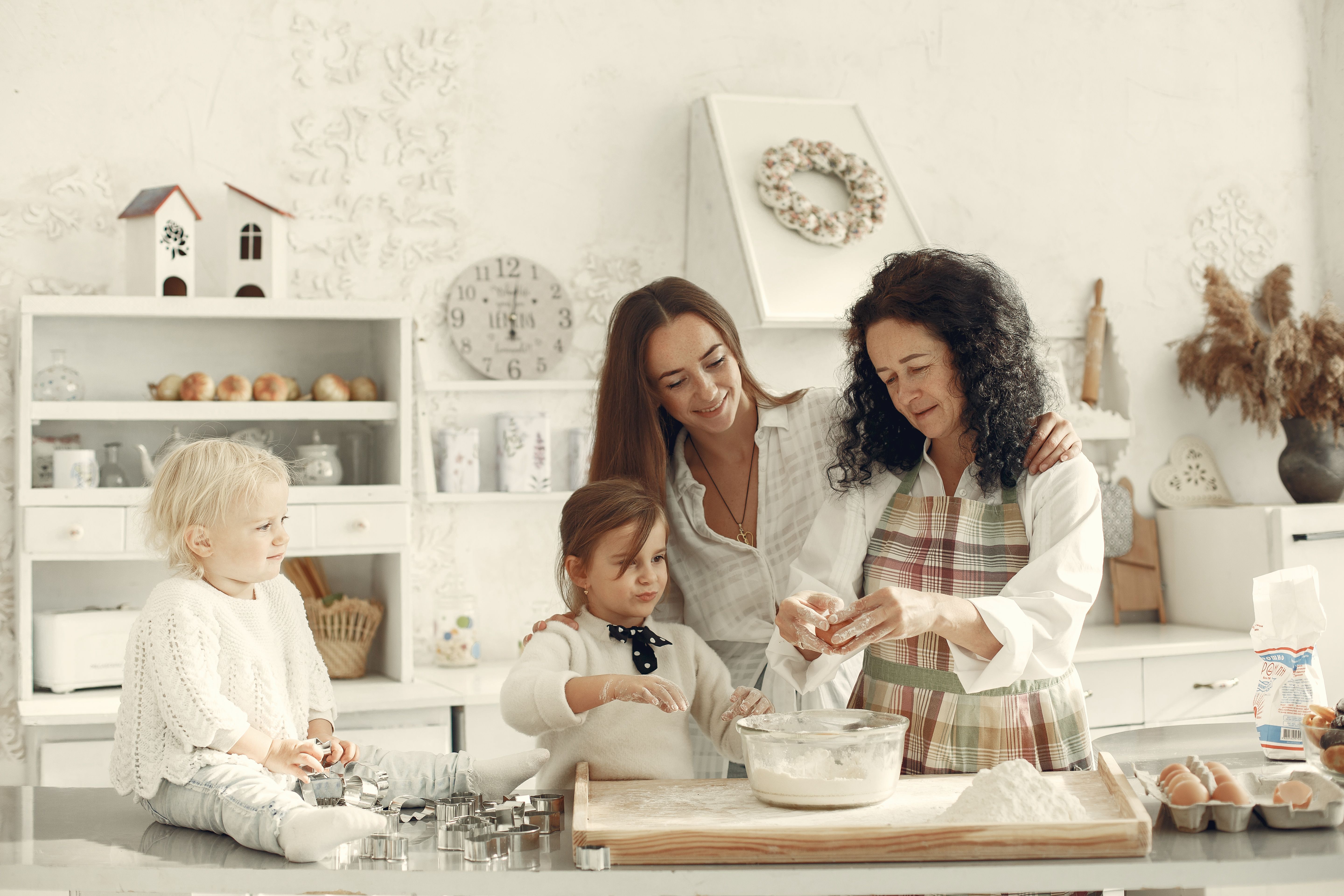 A grandmother, mother, and children baking together in a bright kitchen, enjoying family bonding.