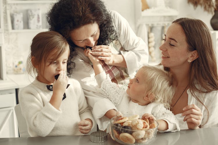 Grandmother, Mother And Two Little Girls In A Kitchen Eating Cookies 