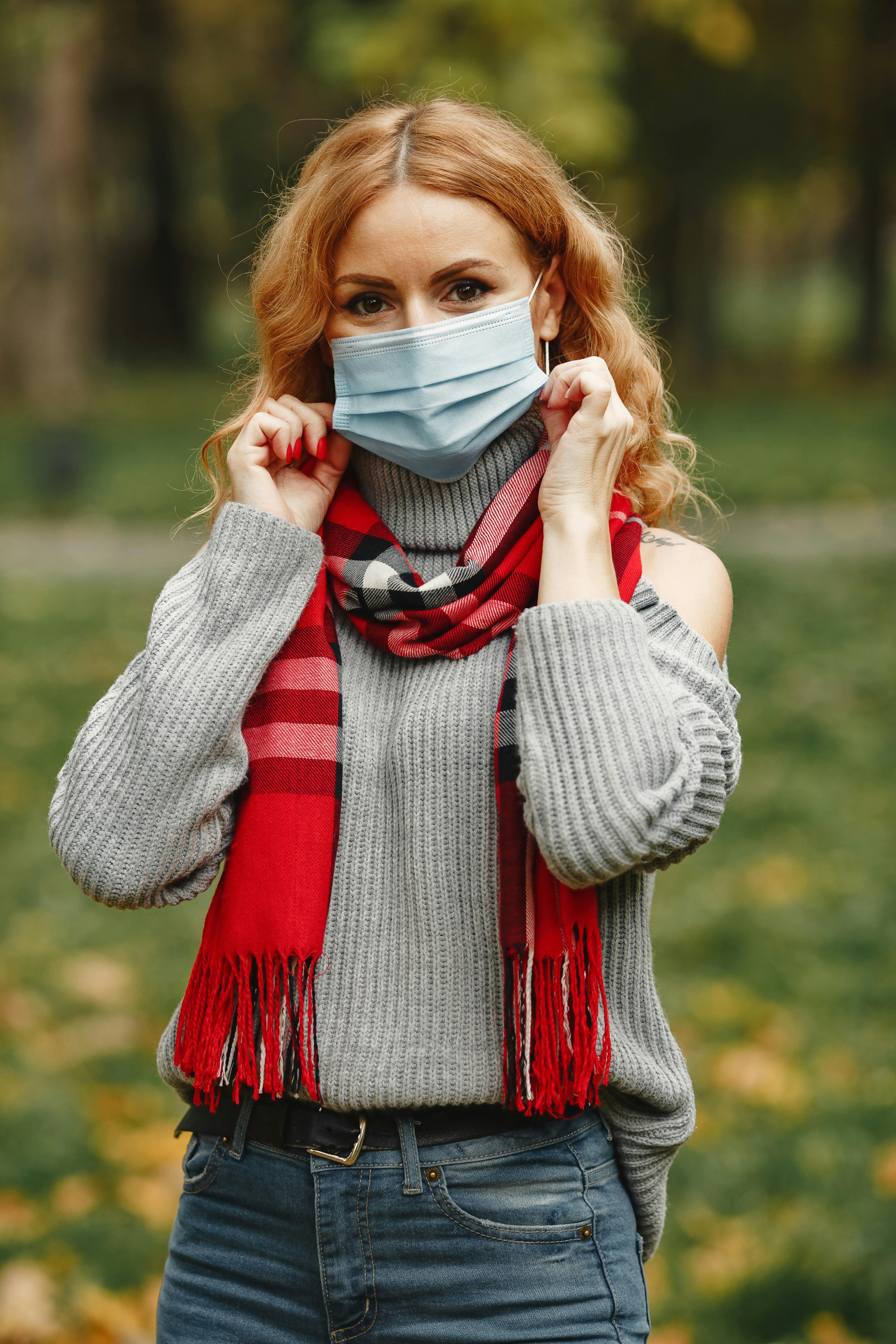 woman in gray knit sweater covering face with white face mask