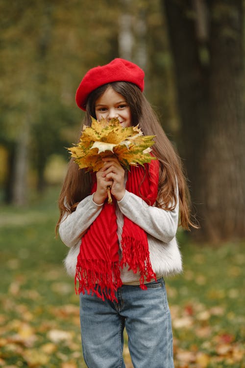 Cute Little Girl in a Red Beret Holding a Bunch of Autumnal Leaves