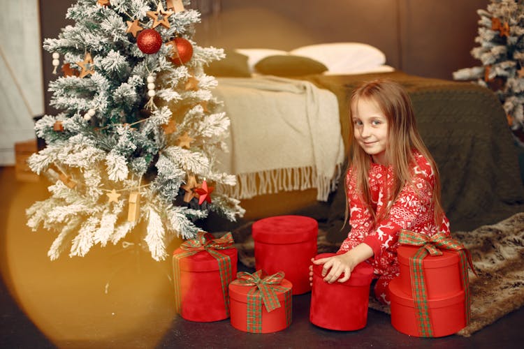 Little Girl Smiling And Opening Presents Under A Christmas Tree