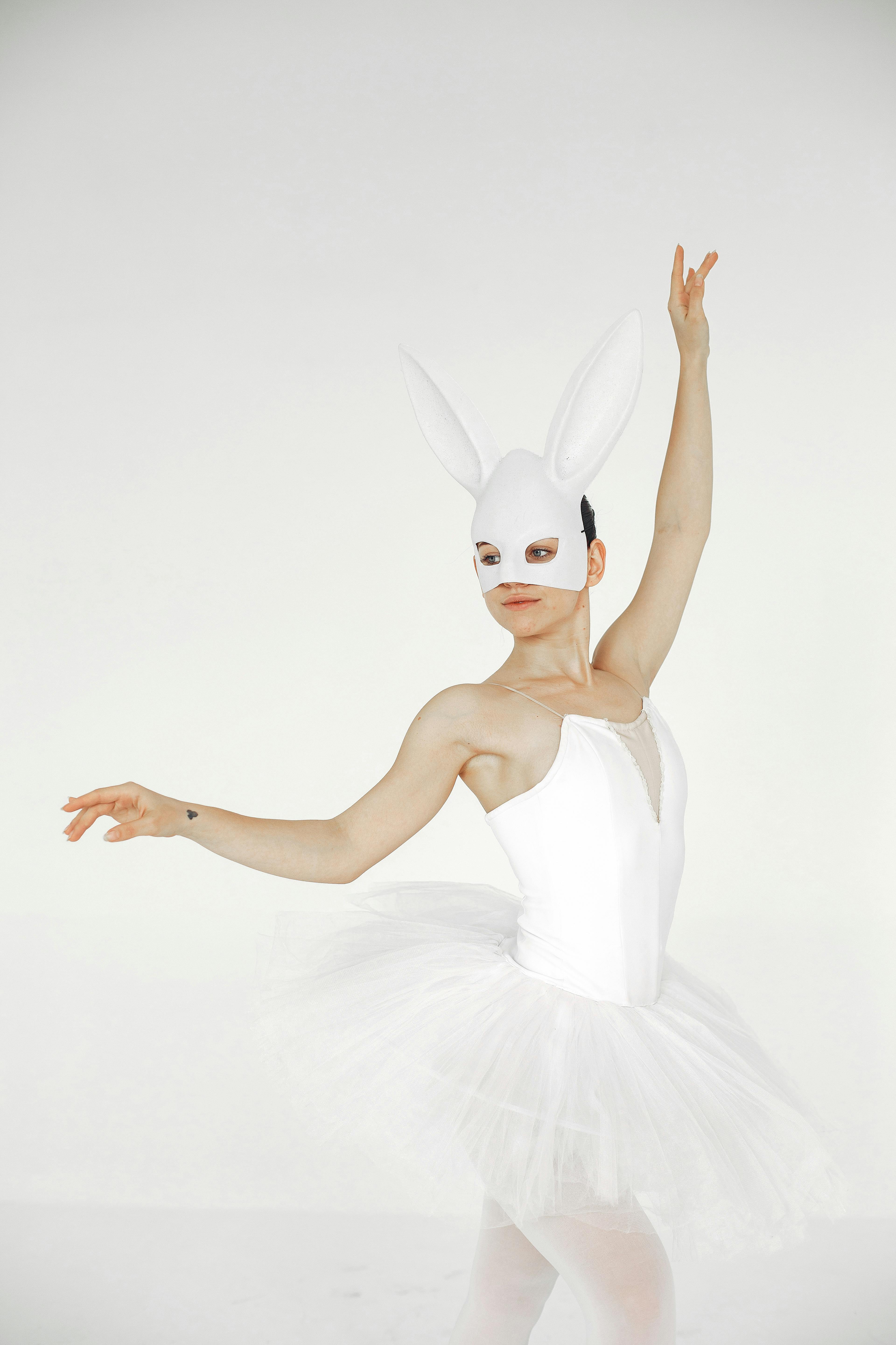 Free Ballet dancer in a white costume and rabbit mask performing gracefully against a neutral background. Stock Photo