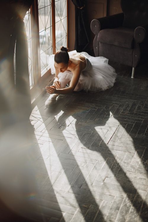 Free Elegant ballerina in a tutu stretching by a window with dramatic light and shadows. Stock Photo