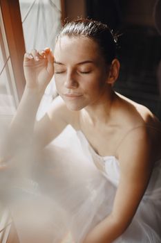 A serene ballerina in a white tutu enjoys a moment of reflection by the window.