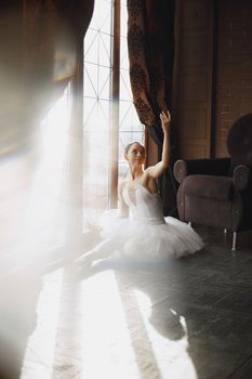 Ballerina sits elegantly on the floor, reaching toward sunlight streaming through a window.