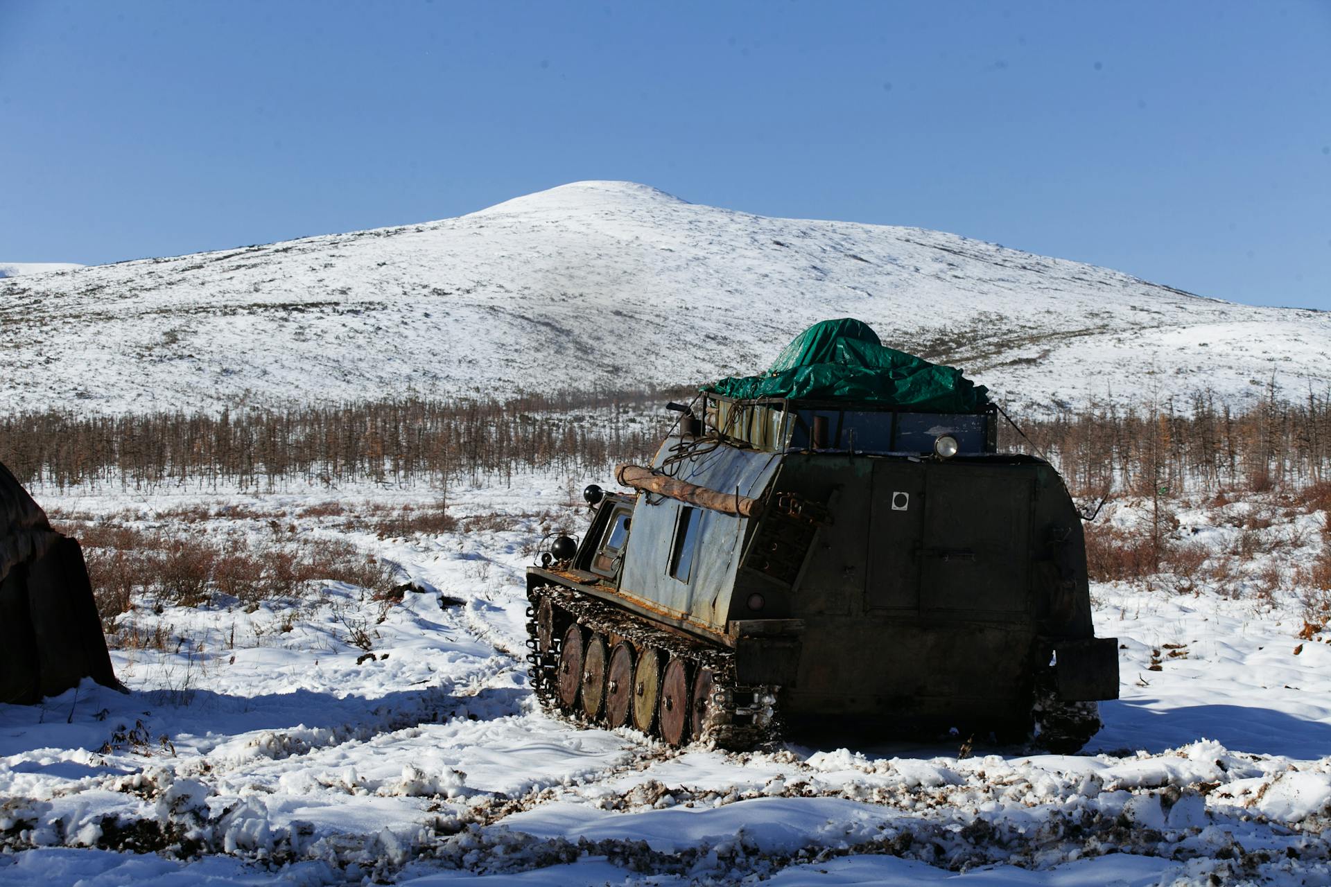 A parked amphibious vehicle in a snow-covered valley under a blue sky.