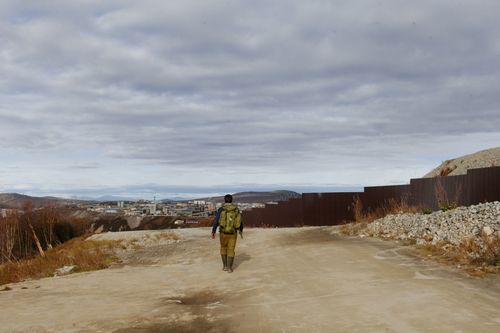 Free Back view of anonymous male with backpack walking in outskirts of city under cloudy sky Stock Photo