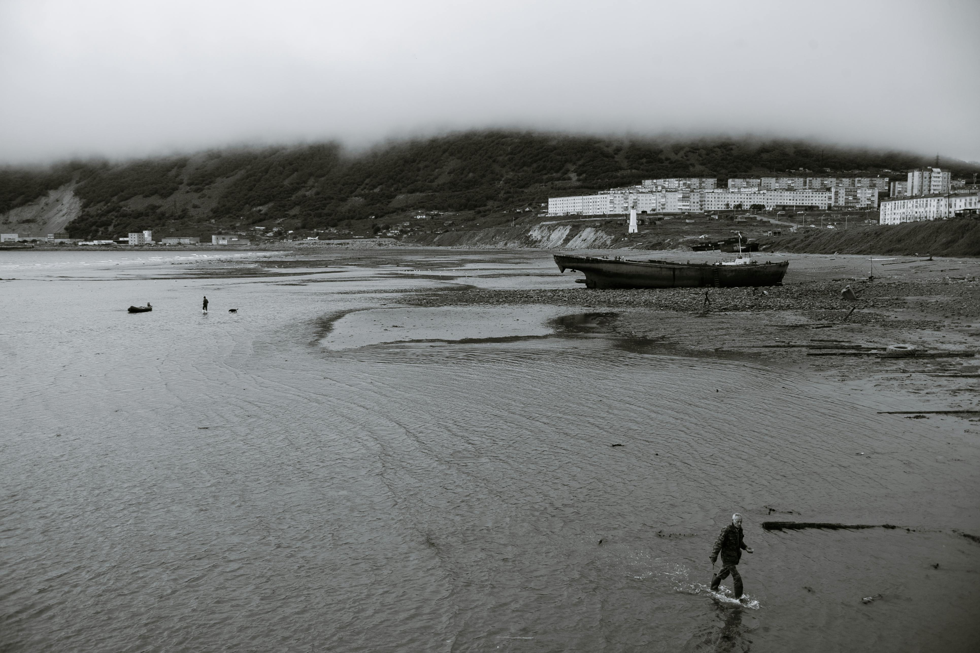 anonymous man walking in sea near coast surrounded by hills on cloudy day