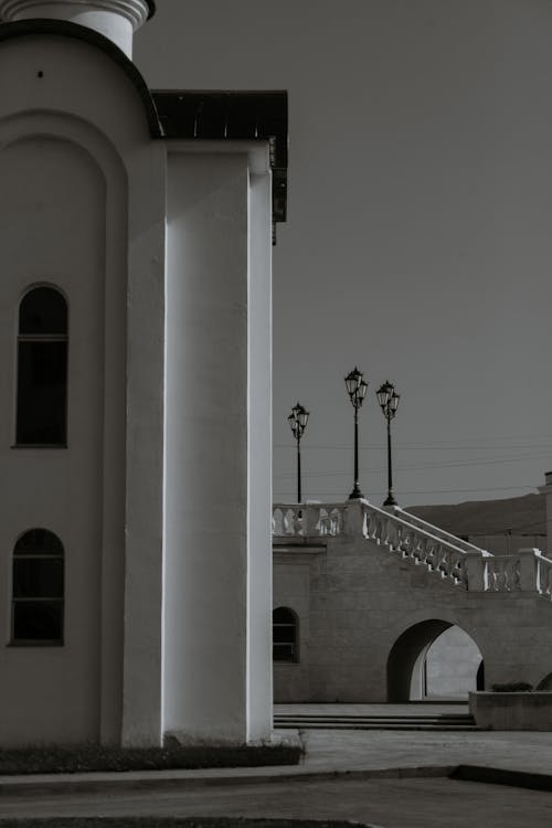 Black and white exterior details of aged Holy Trinity Cathedral with stairway decorated with vintage streetlamps against cloudy sky in Magadan