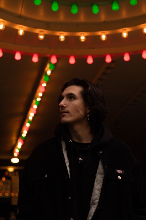 Free Moody portrait of a man standing beneath colorful lights in an indoor setting, capturing a contemplative moment. Stock Photo