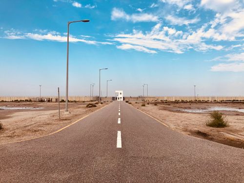 Free An empty asphalt road vanishing into the distance beneath a vibrant blue sky and scattered clouds. Stock Photo