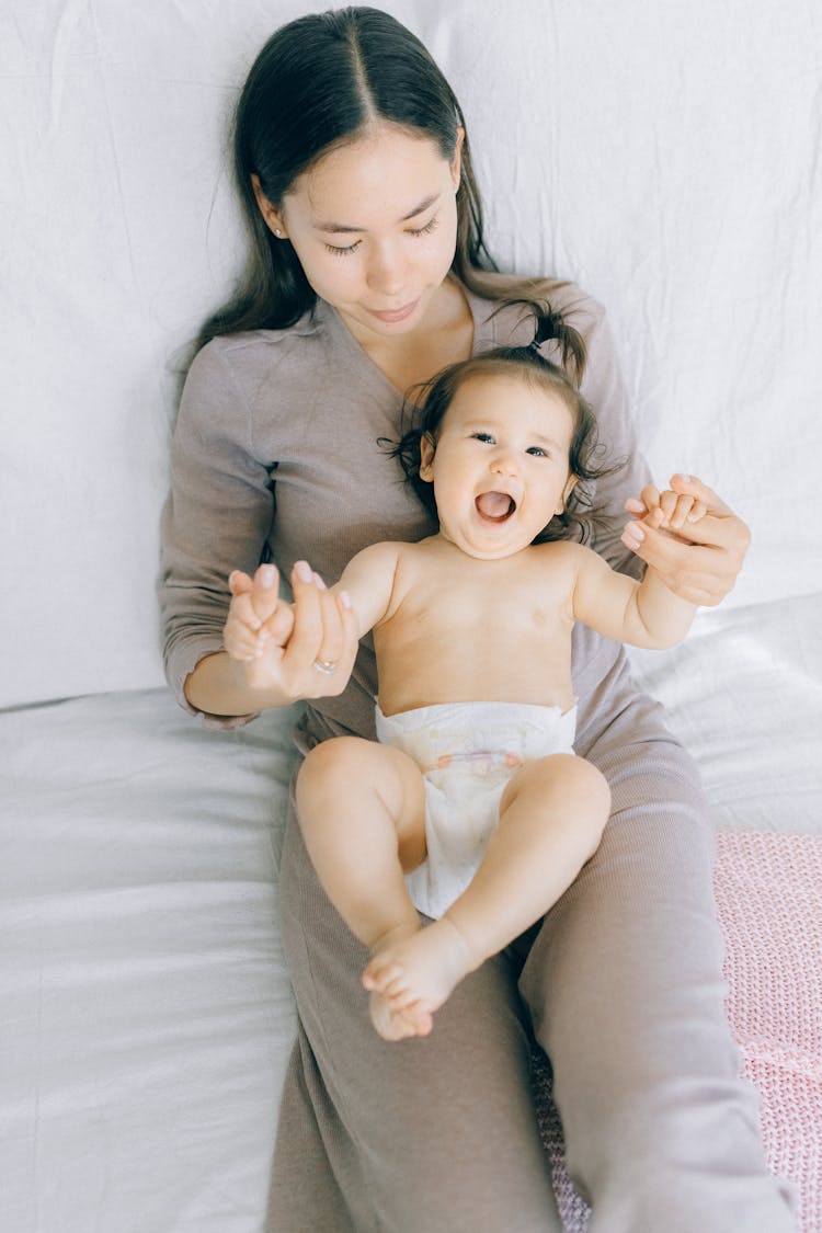 Mother Sitting On Bed Holding A Baby 