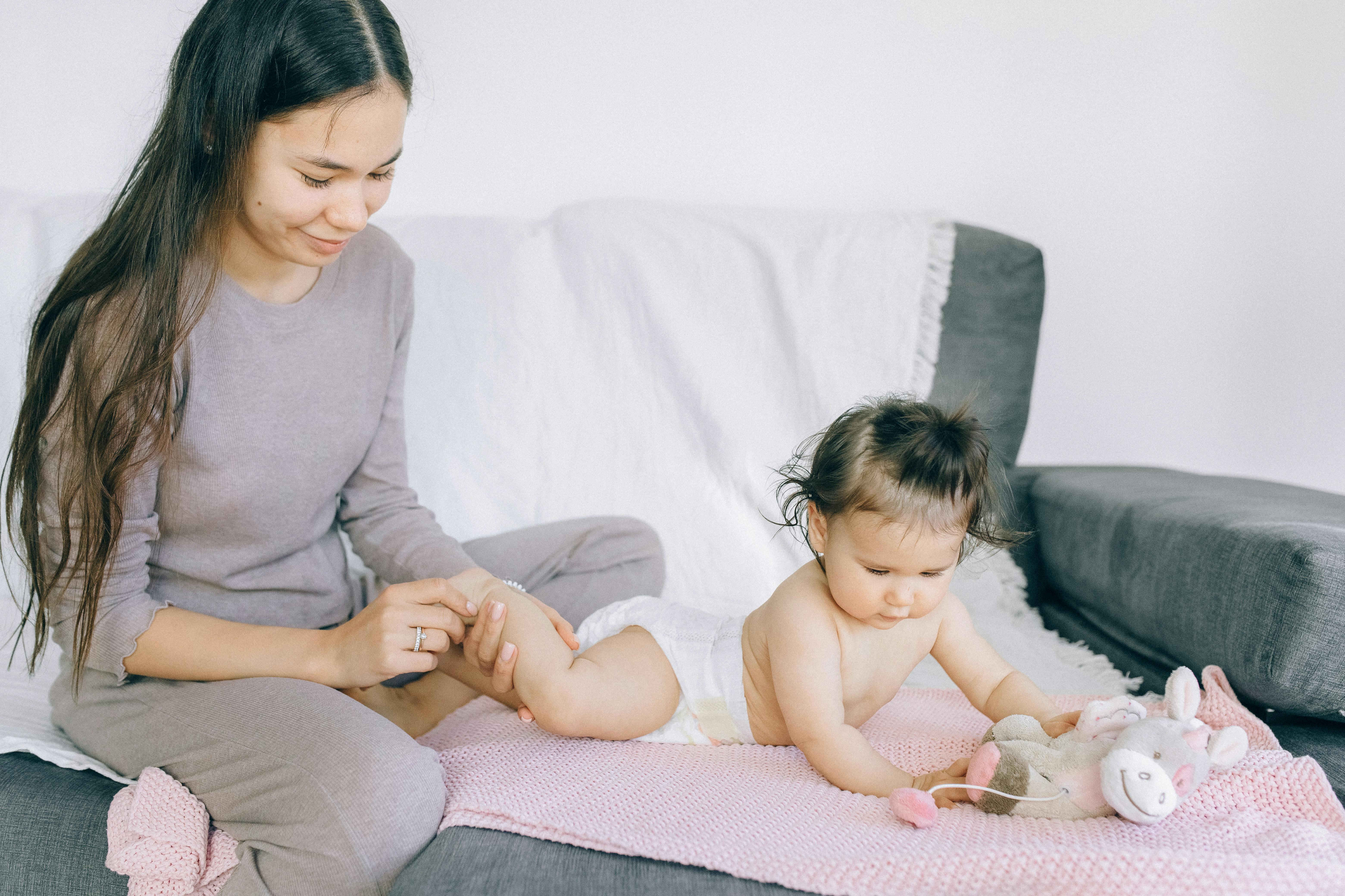 A loving mother gently massaging her baby's leg while the child plays indoors.