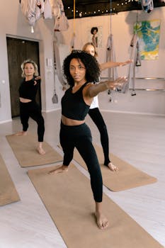 Three women in a yoga class demonstrating warrior pose on mats in a serene studio.