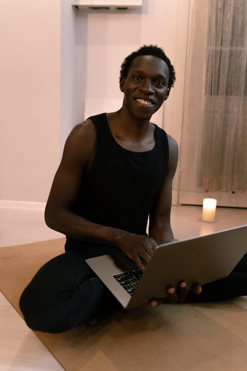 Man in Black Tank Top Smiling While Using a Laptop 